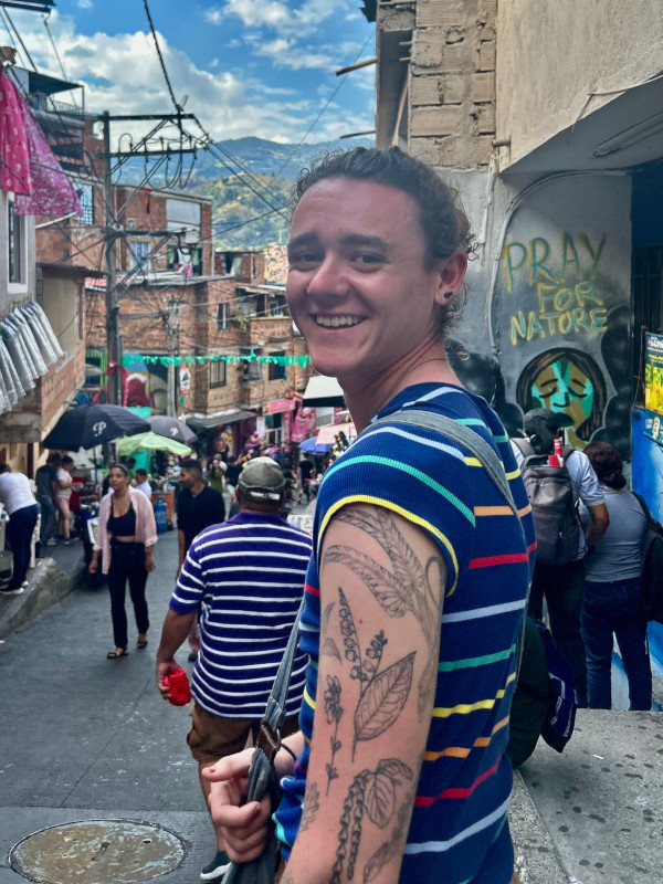 A portrait of Nick in a busy street, with graffiti in the background that reads “pray for nature”.